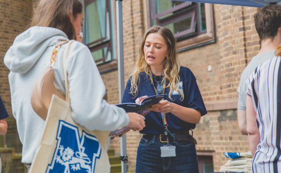 A member of staff shows a prospective student a guide at an open day event